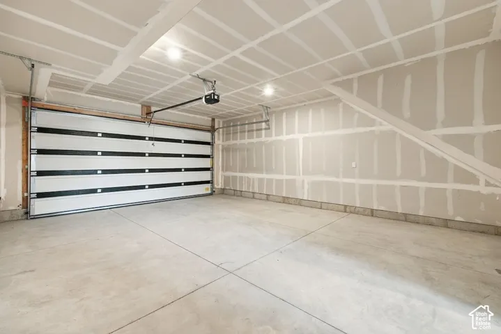 Finished garage featuring concrete flooring, an automated overhead door, recessed lighting, and drywall interior