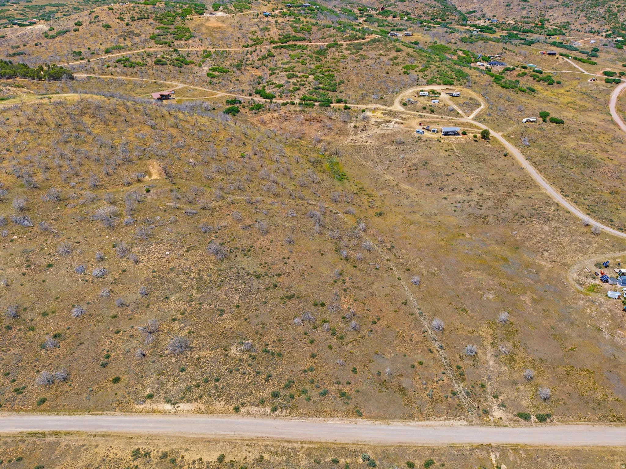 Expansive land featuring a natural, arid landscape with scattered vegetation, visible unpaved roads, and distant structures