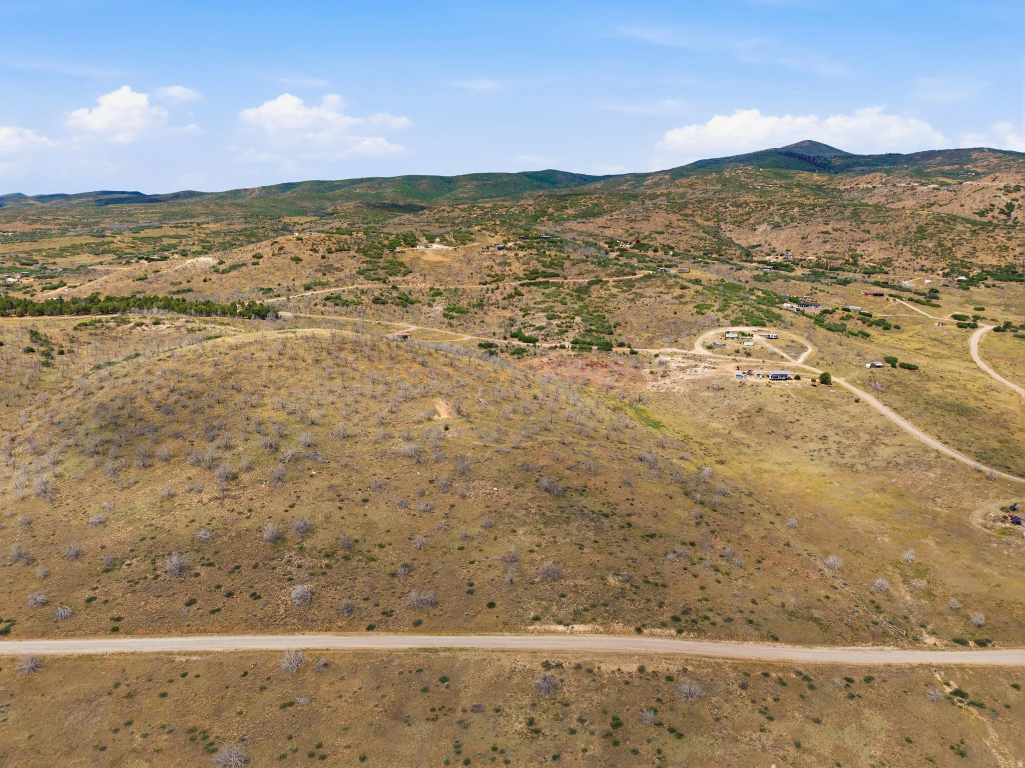 Expansive mountainous terrain featuring scattered vegetation, a visible dirt road, and distant structures nestled within the landscape