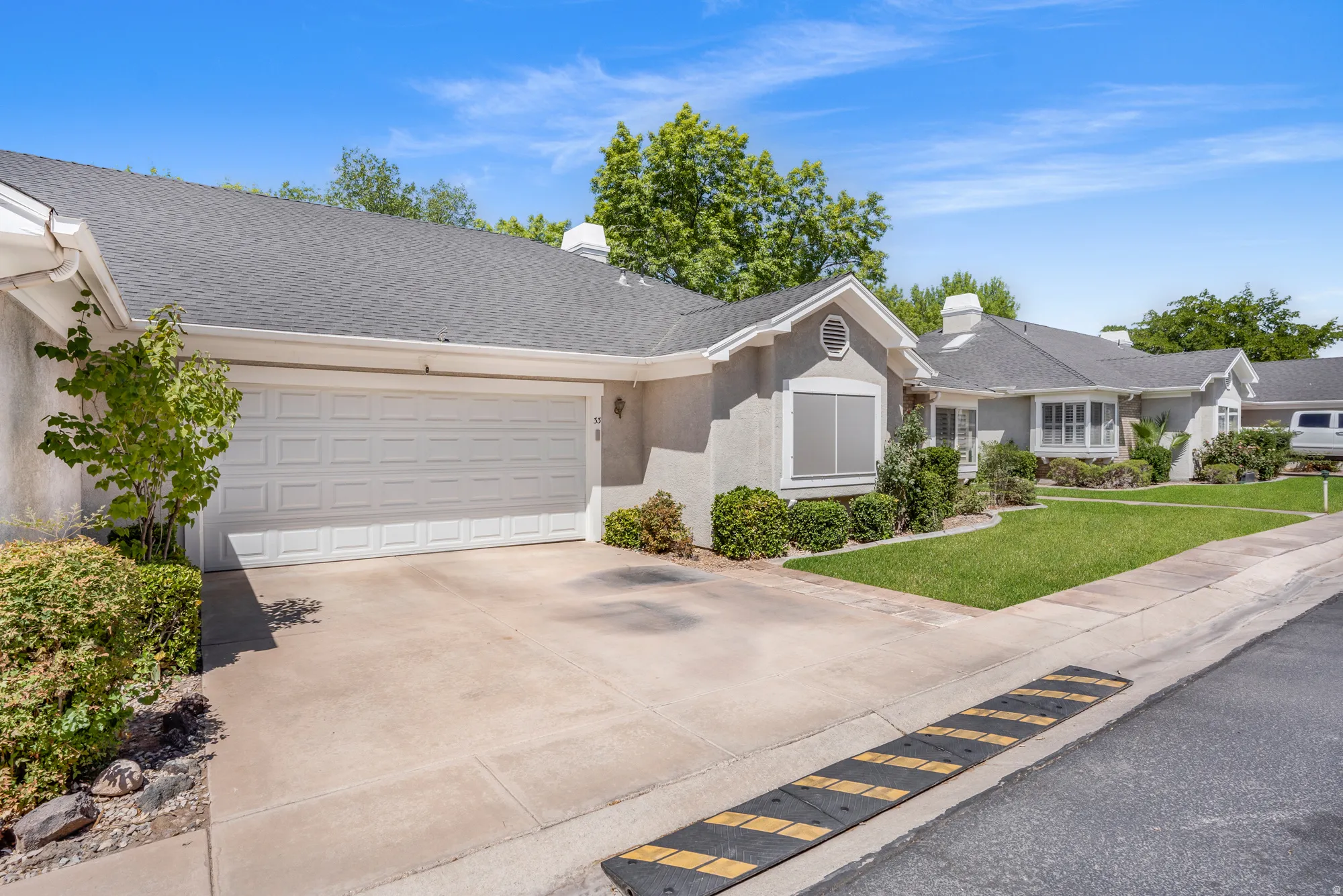 Stucco exterior residence with an attached two-car garage, concrete driveway, and a shingle roof. AI-repaired lawn.