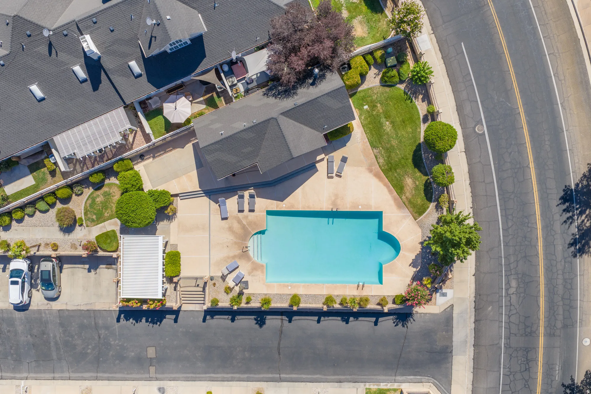 Community swimming pool with a surrounding concrete deck, adjacent to a structured parking area and a landscaped green space