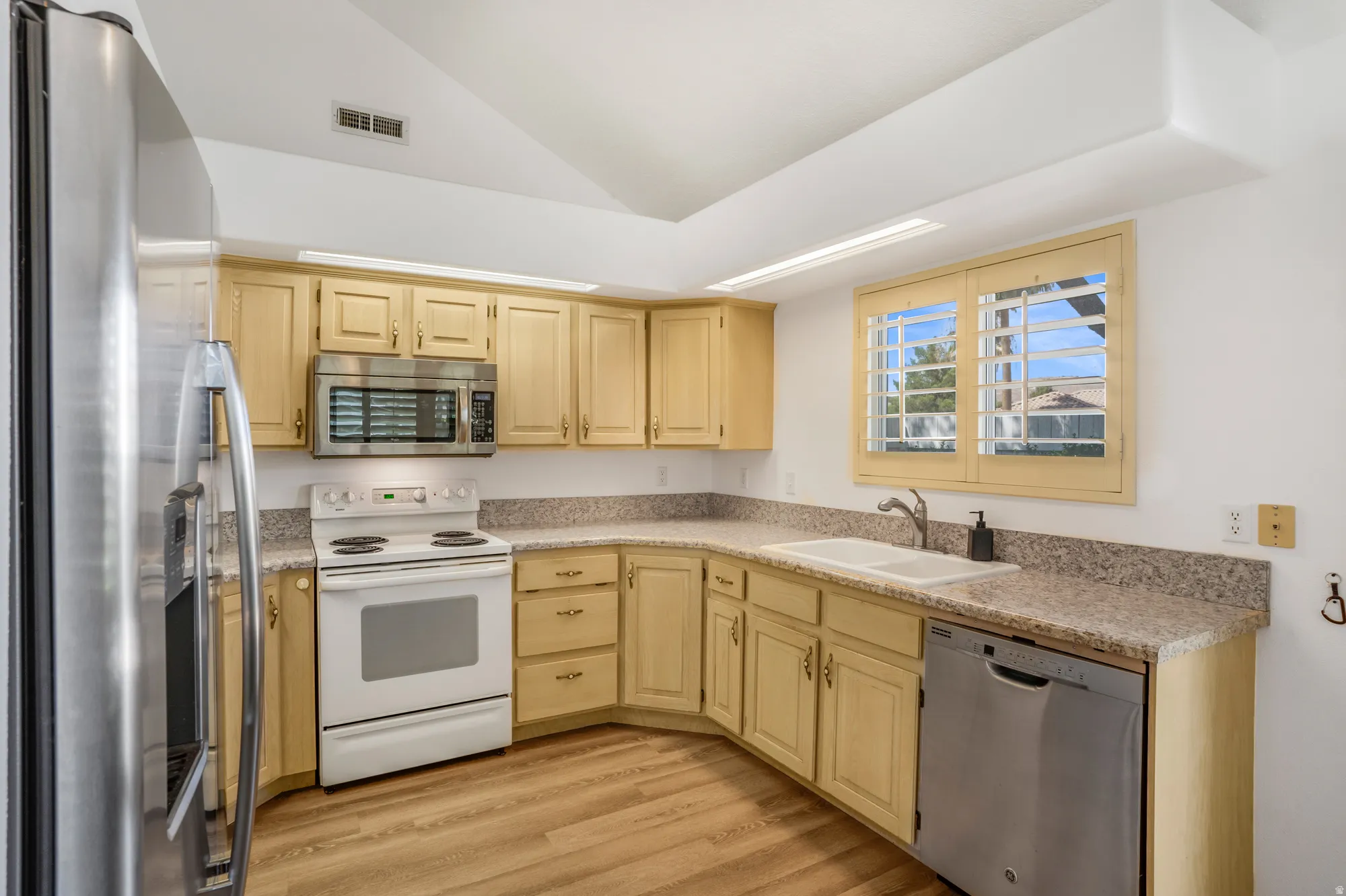 Kitchen featuring light wood cabinetry, granite-finish countertops, stainless steel refrigerator, stainless steel microwave, and wood-finish flooring