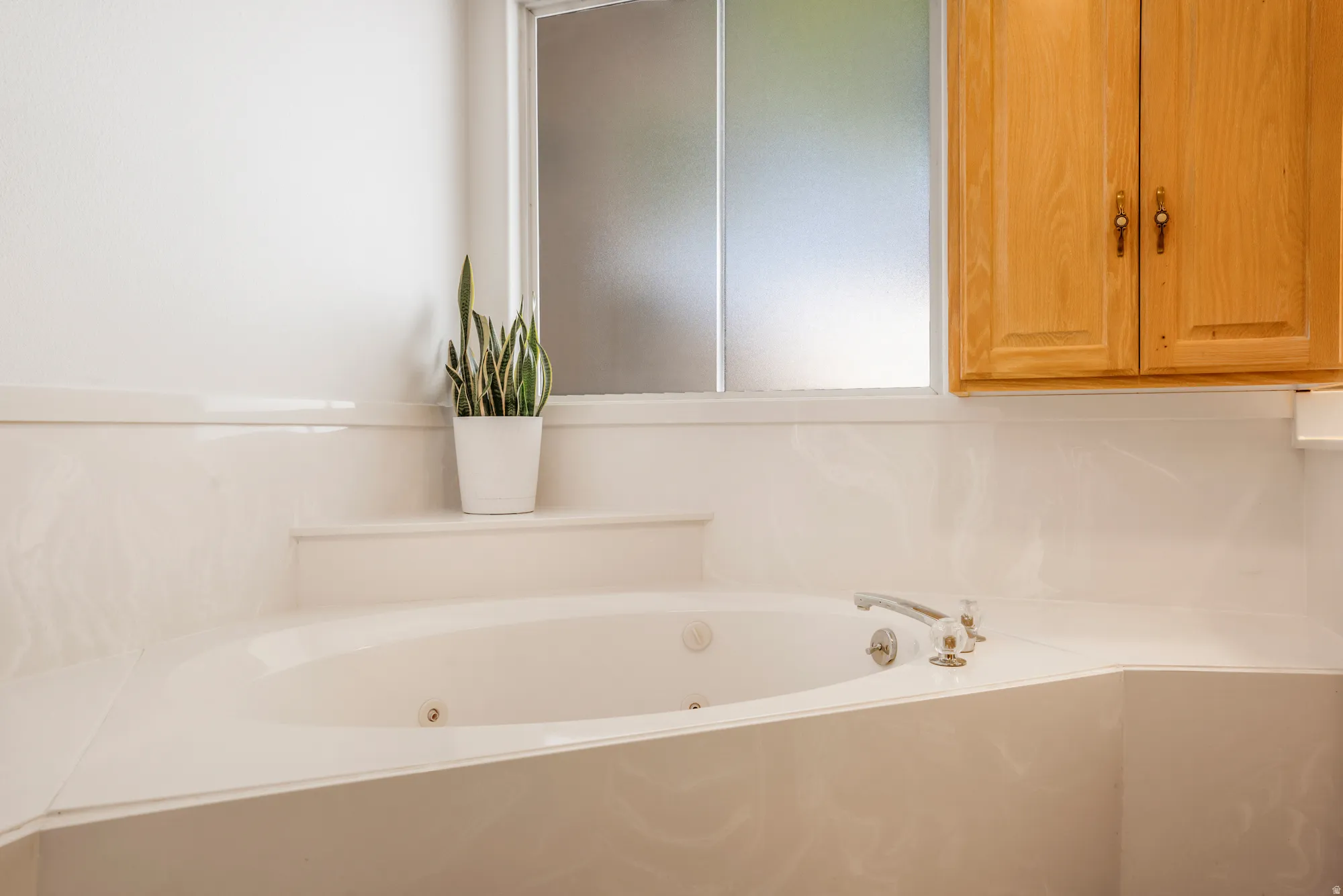 Corner jetted tub featuring a deck-mounted faucet with dual clear acrylic handles