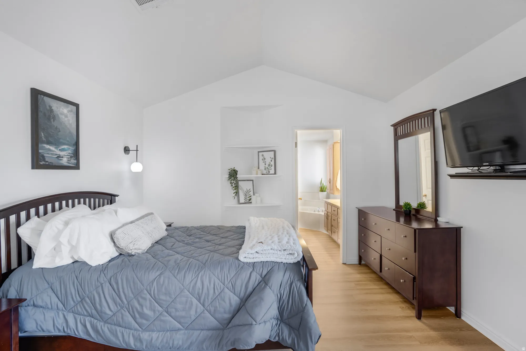 Vaulted ceiling bedroom with light wood-finish flooring
