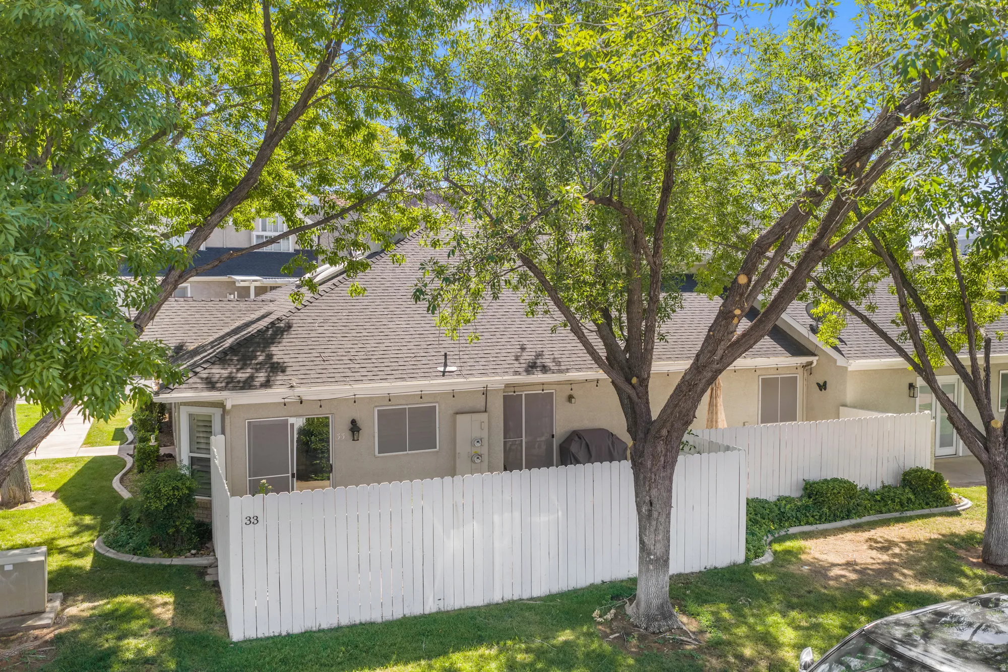 Private fenced patio area featuring a white picket fence, mature trees, and landscaped shrubbery