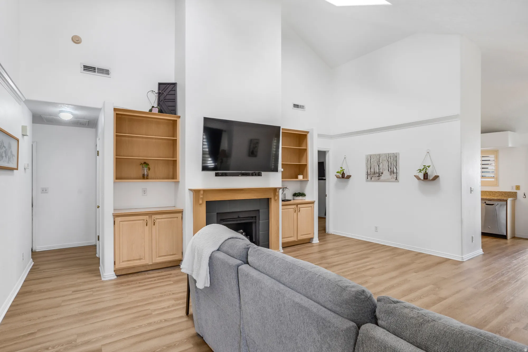 Living area featuring vaulted ceilings, a central fireplace with a wood mantle, built-in shelving, wood-finish flooring, and a skylight
