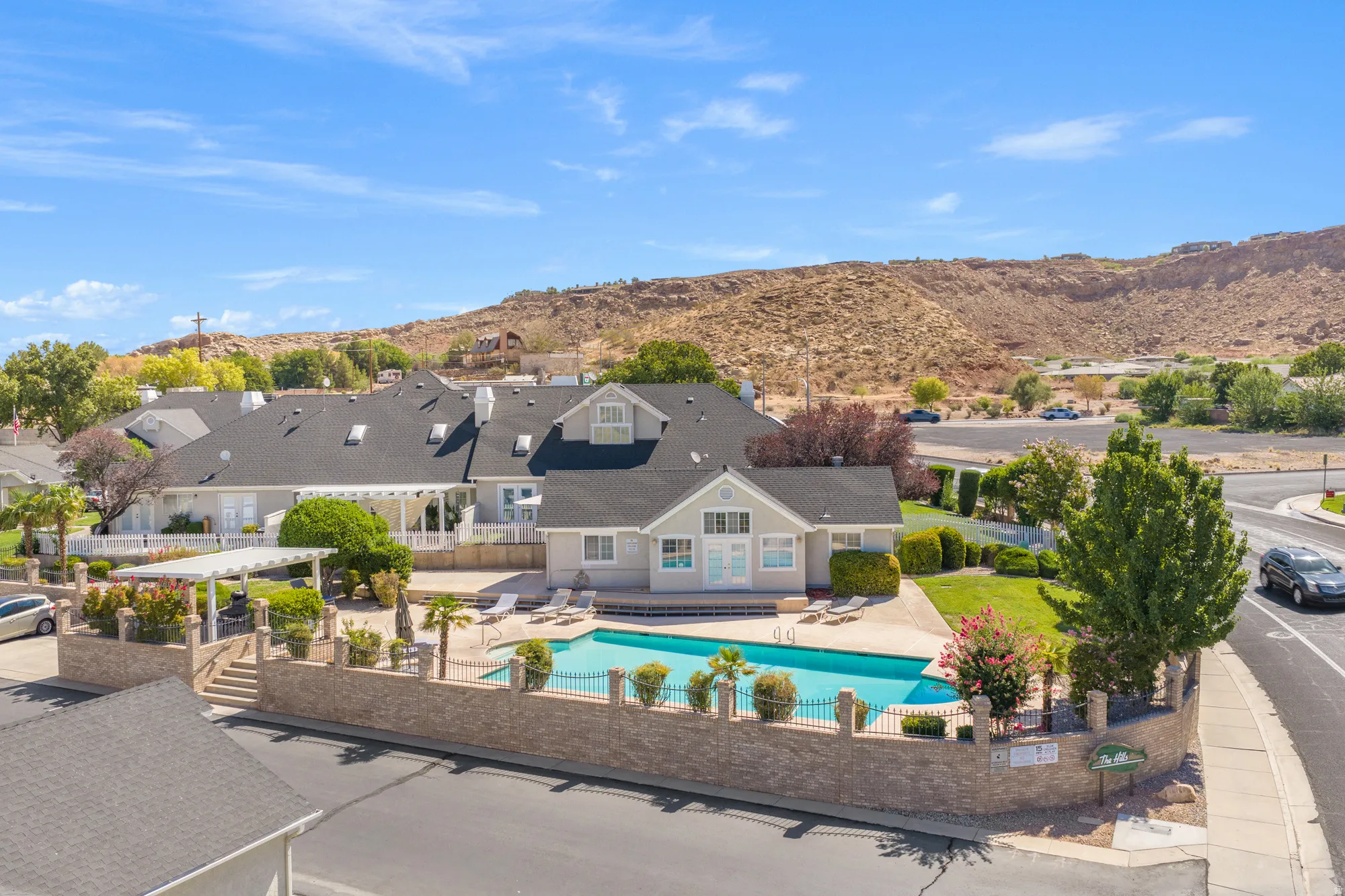 Community swimming pool with surrounding patio space, a decorative stone wall, and established landscaping