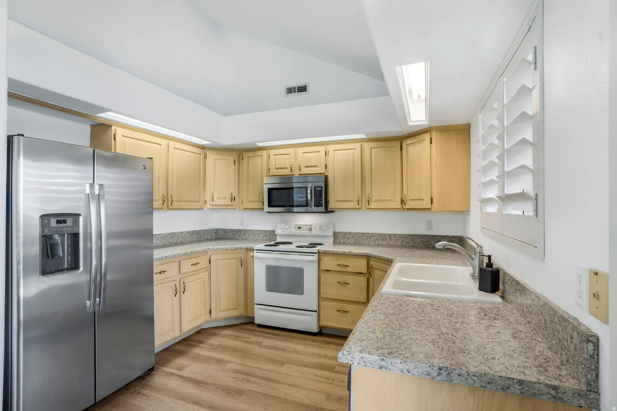 Kitchen featuring wood-finish flooring, light wood cabinetry, stone-look countertops, and a double basin sink with a contemporary faucet