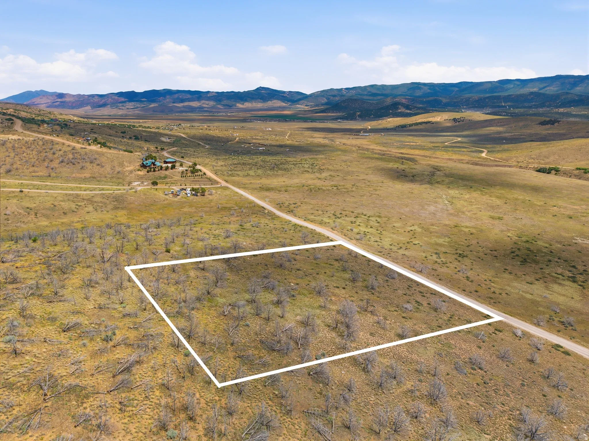 Expansive undeveloped land featuring a clear parcel boundary, direct road frontage, and distant mountain vistas