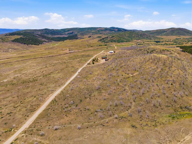 Expansive rural property featuring a long gravel driveway, a single-story dwelling, and a secondary structure nestled within a vast, open landscape with rolling hills and distant mountainous terrain