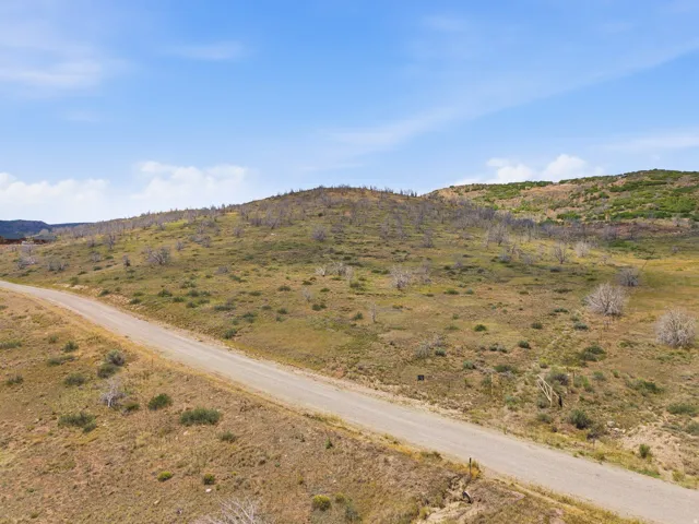 Expansive hillside property featuring a gravel road, varied terrain, and distant structures