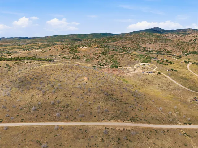 Expansive mountainous terrain featuring scattered vegetation, a visible dirt road, and distant structures nestled within the landscape