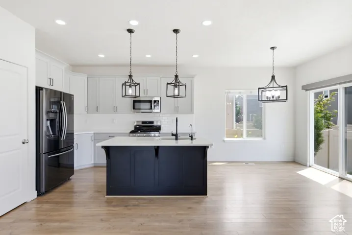 Open-concept kitchen featuring light wood-finish flooring, a central island with a solid surface countertop, white cabinetry with modern hardware, a black appliance suite, and a sliding glass door