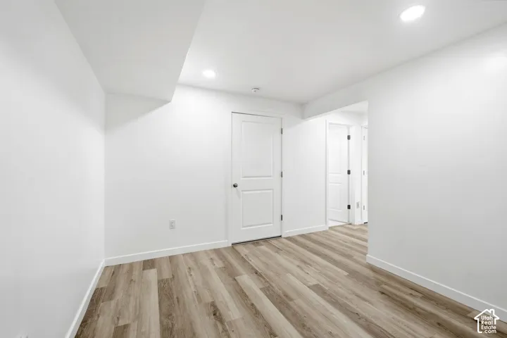 Spacious room featuring wood-finish flooring, recessed lighting, white walls, and white trim