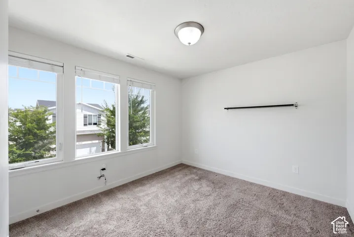 Bright interior space featuring three large windows, white walls, and neutral-toned carpet