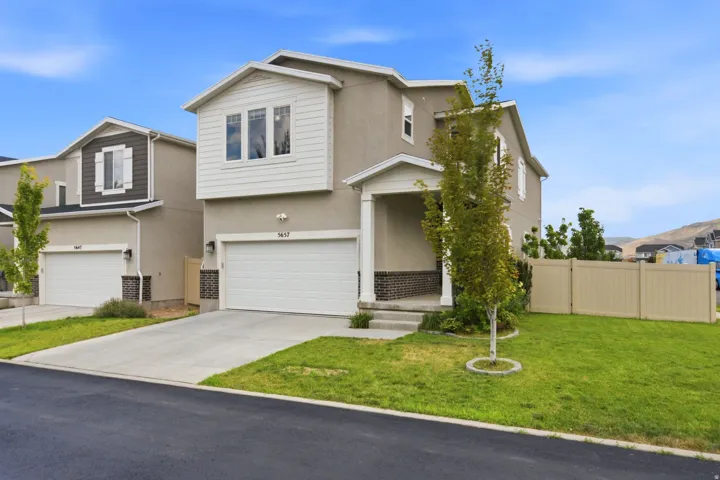 Contemporary two-story residence featuring a covered front porch, an attached two-car garage with a concrete driveway, and a tan privacy fence enclosing a portion of the property