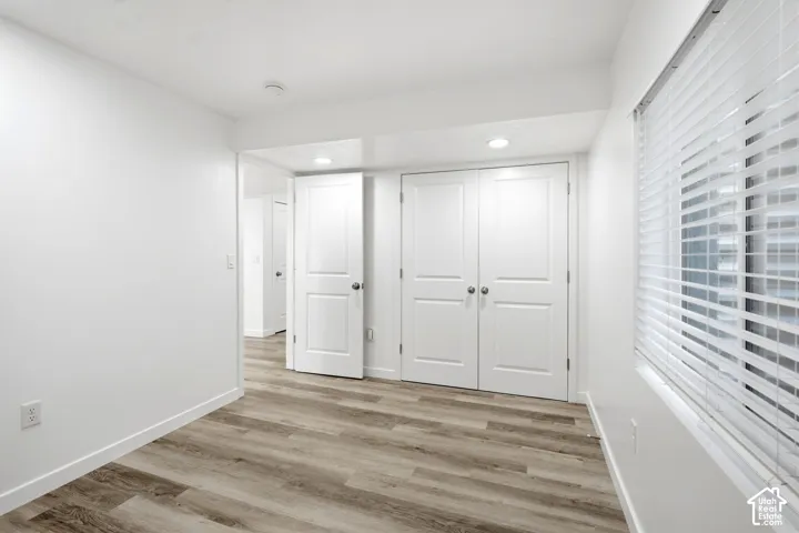Room featuring wood-finish flooring, crisp white walls, and a window with horizontal blinds