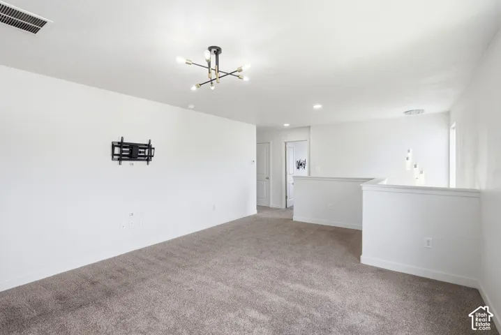 Spacious carpeted area featuring a modern chandelier, recessed lighting, white painted walls, and a built-in wall mount