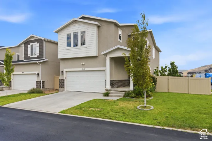 Contemporary two-story residence featuring a covered front porch, an attached two-car garage with a concrete driveway, and a tan privacy fence enclosing a portion of the property