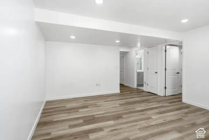 Spacious room featuring wood-finish flooring, recessed lighting, white baseboards, and white walls