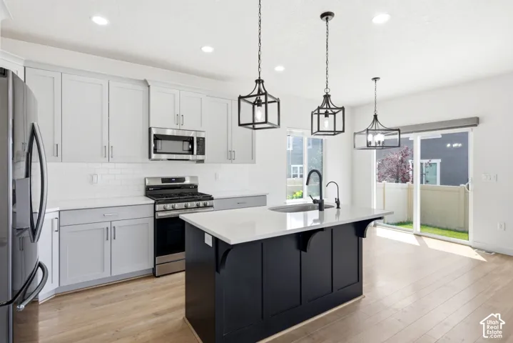 Modern kitchen featuring light gray cabinetry, stainless steel appliances, a white subway tile backsplash, and light wood-finish flooring