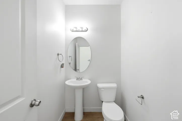 Pedestal sink with an oval mirror, three-light vanity fixture, and white toilet