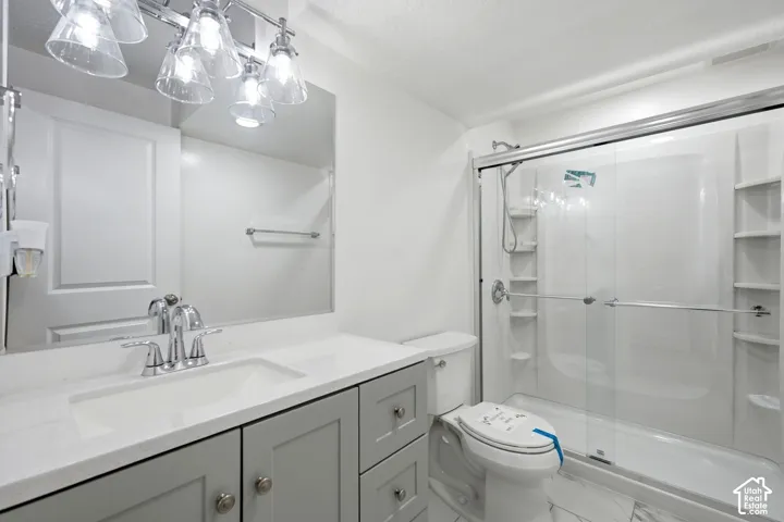 Bathroom featuring a glass-enclosed shower with integrated shelving, a gray vanity with a white countertop and undermount sink, a chrome faucet, and a large wall-mounted mirror