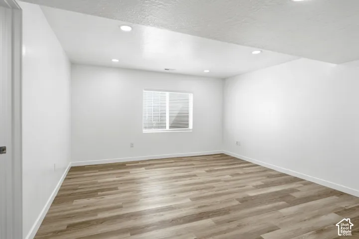 Spacious room featuring wood-finish flooring, recessed ceiling lighting, a window with horizontal blinds, and clean white walls with matching baseboards