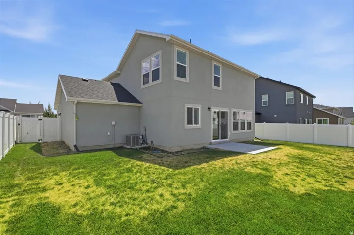 Spacious backyard featuring a concrete patio, vinyl fencing, and a side gate