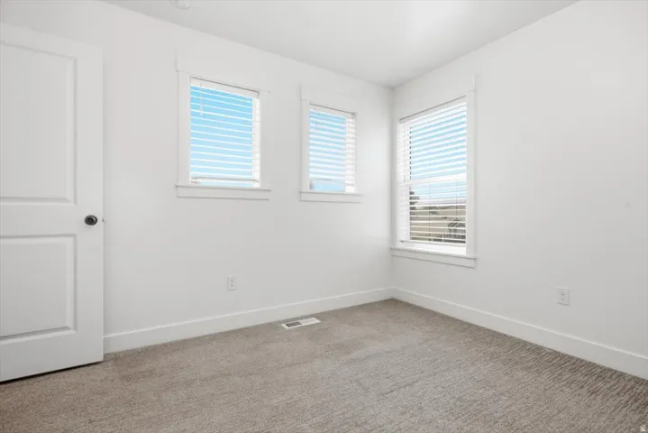 Bright room with multiple windows featuring white blinds, neutral carpeting, and white baseboards