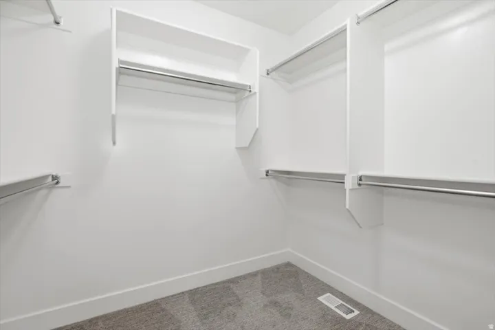 Walk-in closet featuring white walls, white shelving, multiple chrome hanging rods, white baseboards, and grey carpet flooring