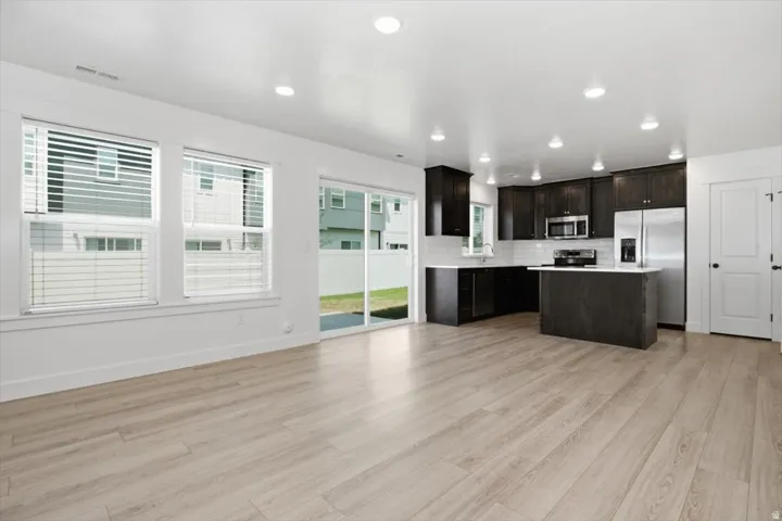 Open-concept living space featuring wood-finish flooring, recessed lighting, and large windows with blinds
