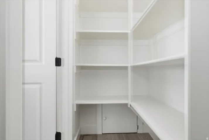 Corner pantry featuring extensive white shelving, wood-finish flooring, and a white paneled door with dark hardware