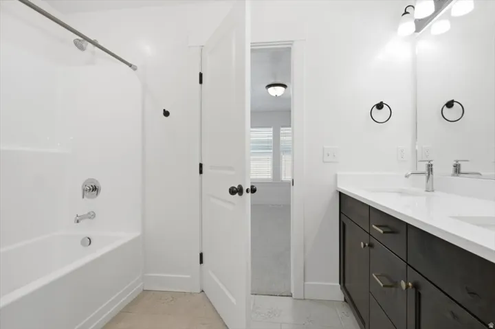 Bathroom featuring a dark wood-finish double vanity with a light-colored countertop, chrome fixtures, a built-in bathtub with shower, and tile flooring