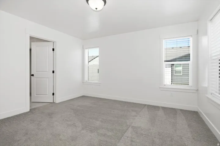 Bright interior space featuring light gray carpeting, crisp white walls, and two windows with horizontal blinds