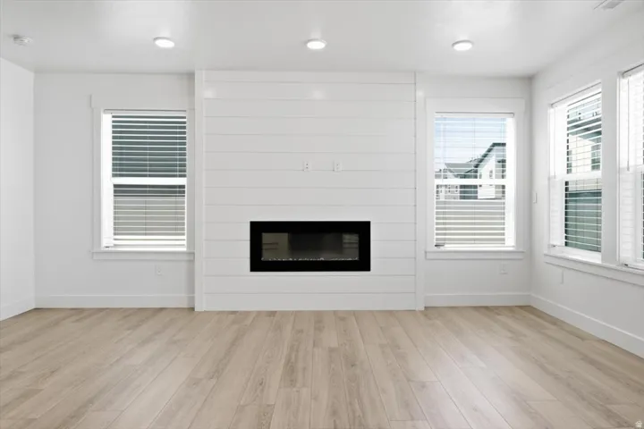 Living area featuring a shiplap accent wall with an inset electric fireplace, recessed lighting, wood-finish flooring, and multiple windows with blinds
