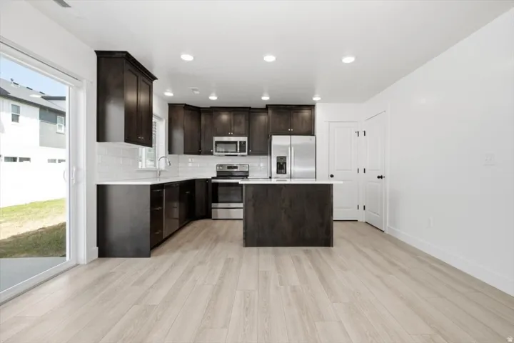 Modern kitchen featuring dark wood-finish cabinetry, stainless steel appliances, a center island, white subway tile backsplash, and light wood-finish flooring