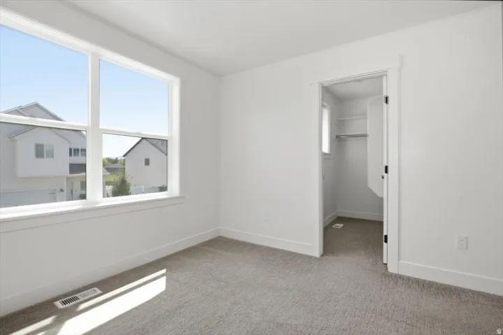 Light-filled room featuring a large window, neutral carpeting, white walls, and a walk-in closet with shelving and hanging rod