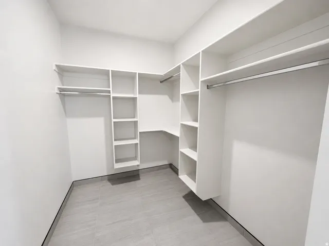 Walk-in closet featuring built-in white shelving, multiple hanging rods, and gray tile flooring