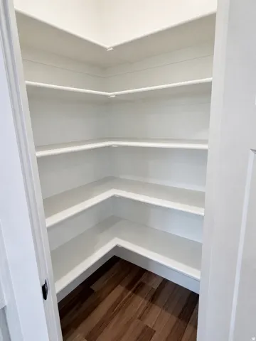 Walk-in pantry featuring white shelving, wood-finish flooring, and a white interior door with dark hardware