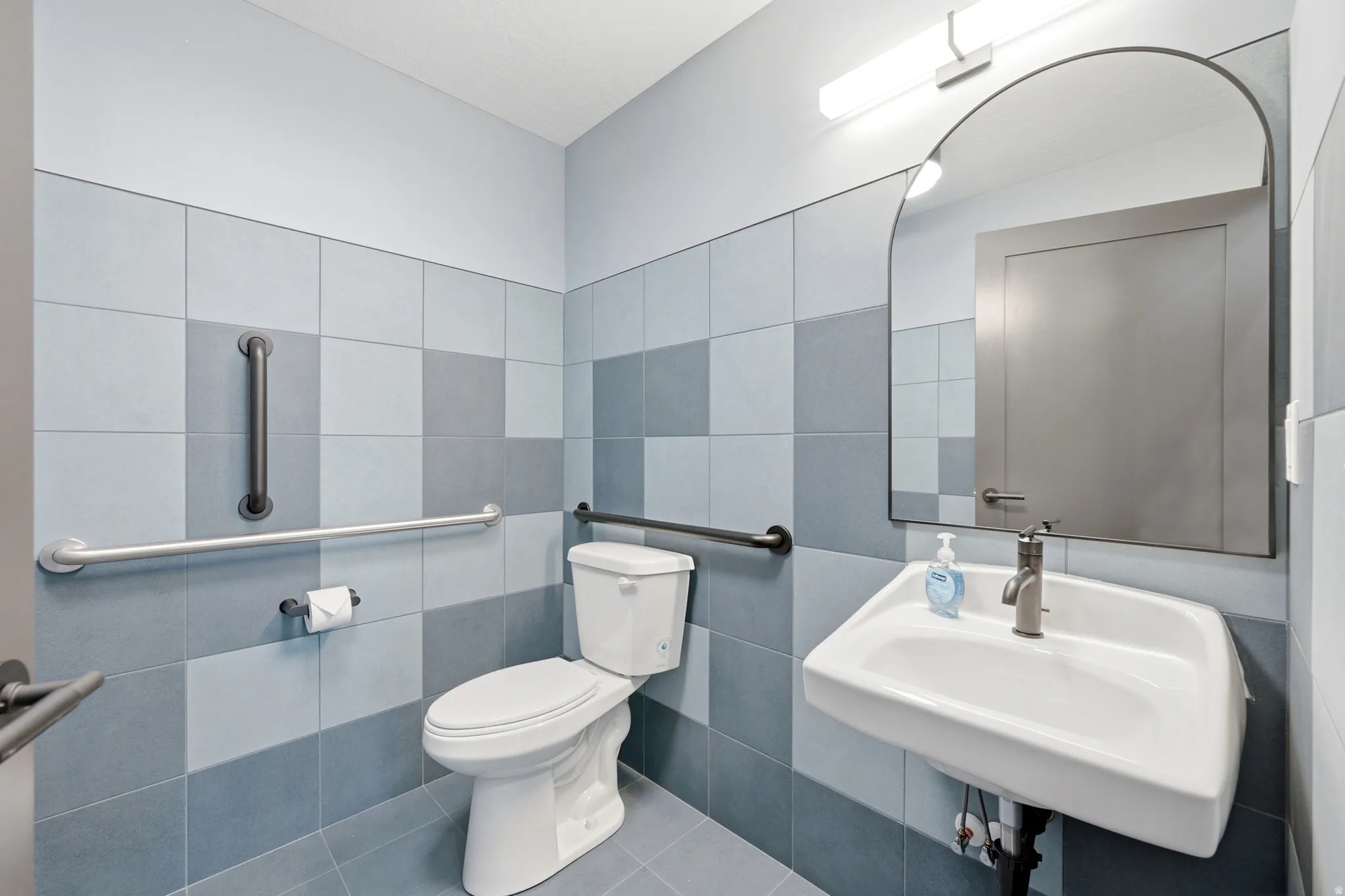 Wall-mounted sink with brushed nickel faucet, arched mirror, and white toilet