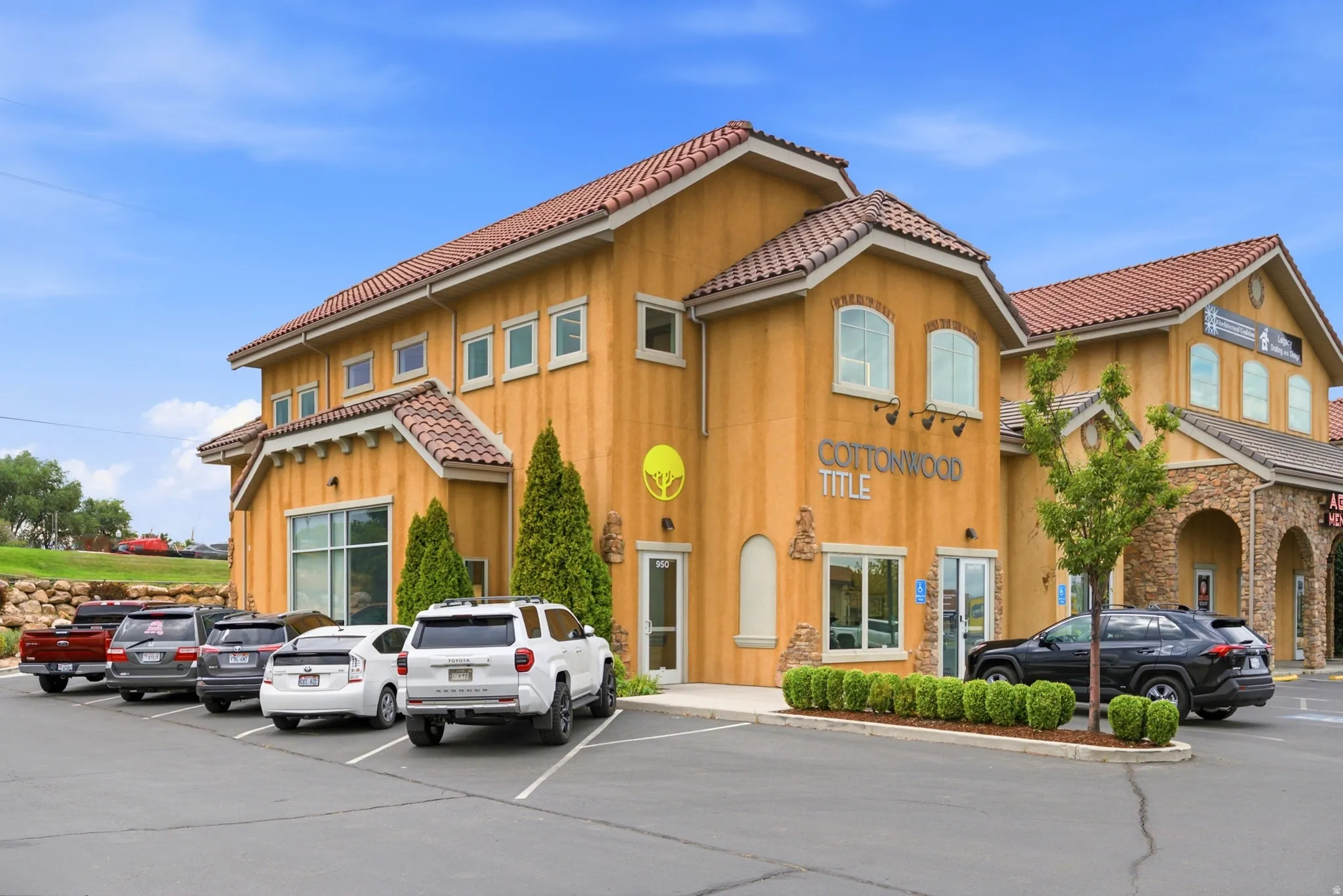 Commercial building with stucco exterior, terra cotta roof tiles, multiple windows, and an asphalt parking area