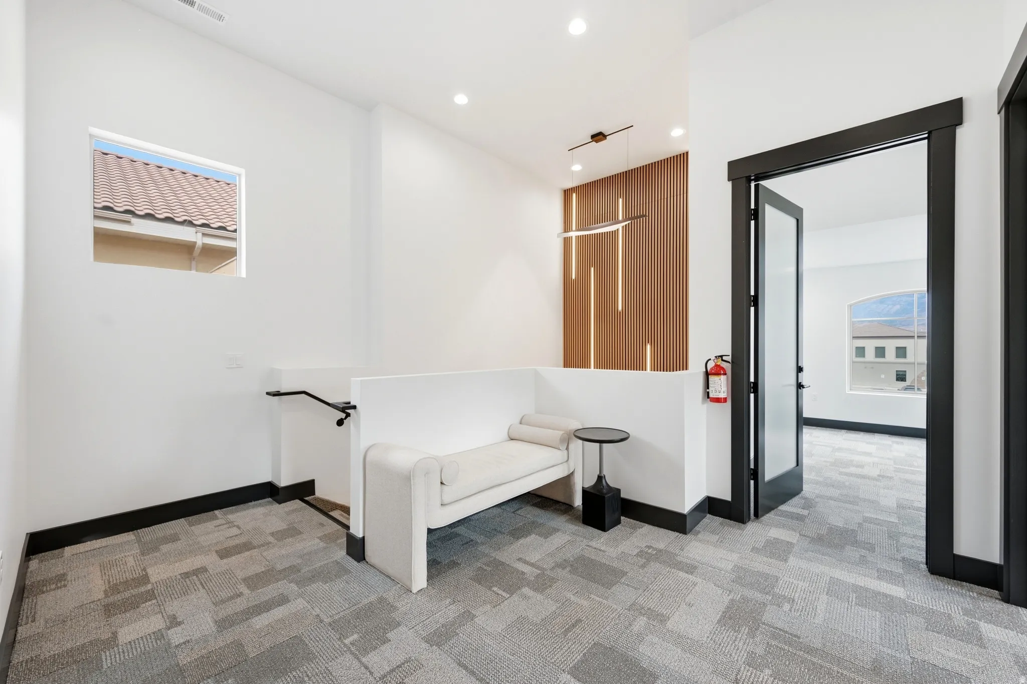 Modern lighting fixture, wood-finish accent wall, dark trim, frosted glass door, and patterned carpet flooring