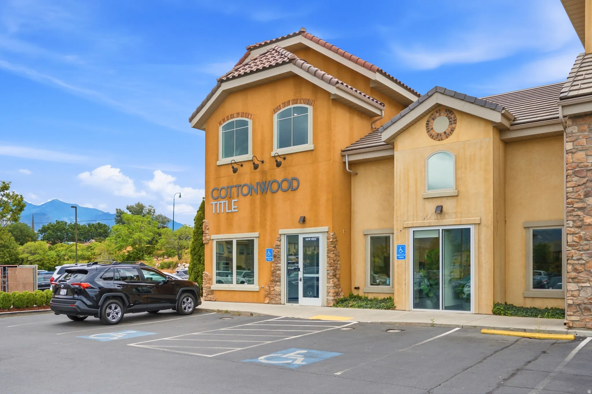 Stucco exterior with stone accents, tile roofing, multiple arched windows, and a dedicated paved parking area