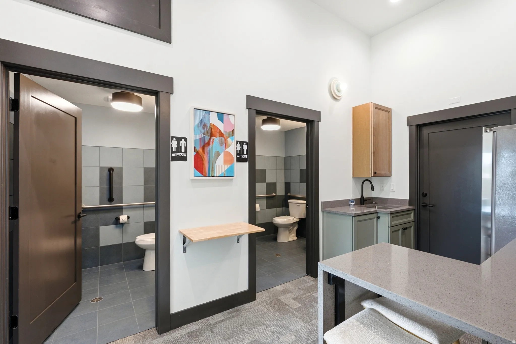 Restroom facilities featuring tile flooring, wall-mounted grab bar, and modern lighting