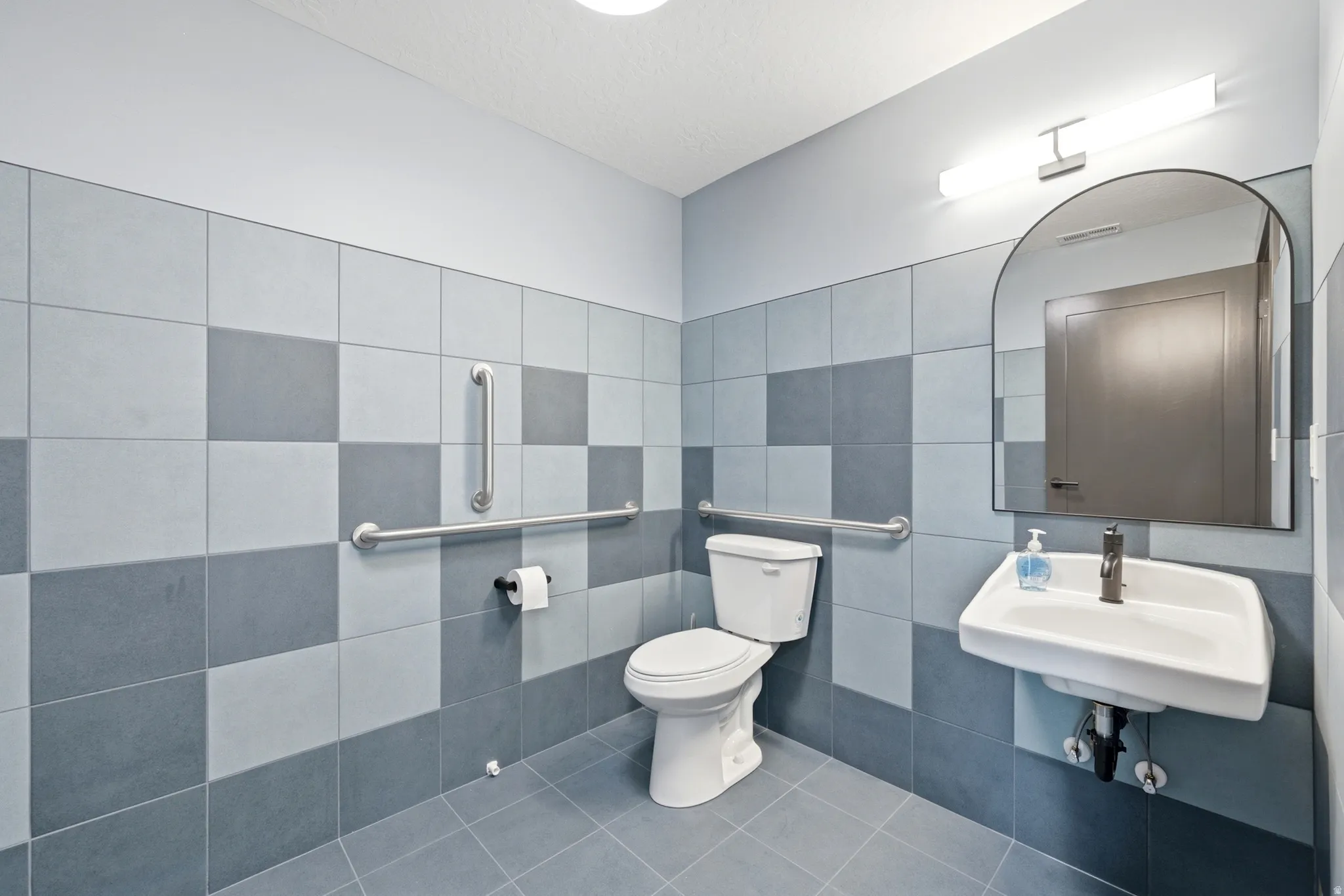 Wall-mounted sink with a matte black faucet, complementary arched mirror, and checkerboard wall tiling