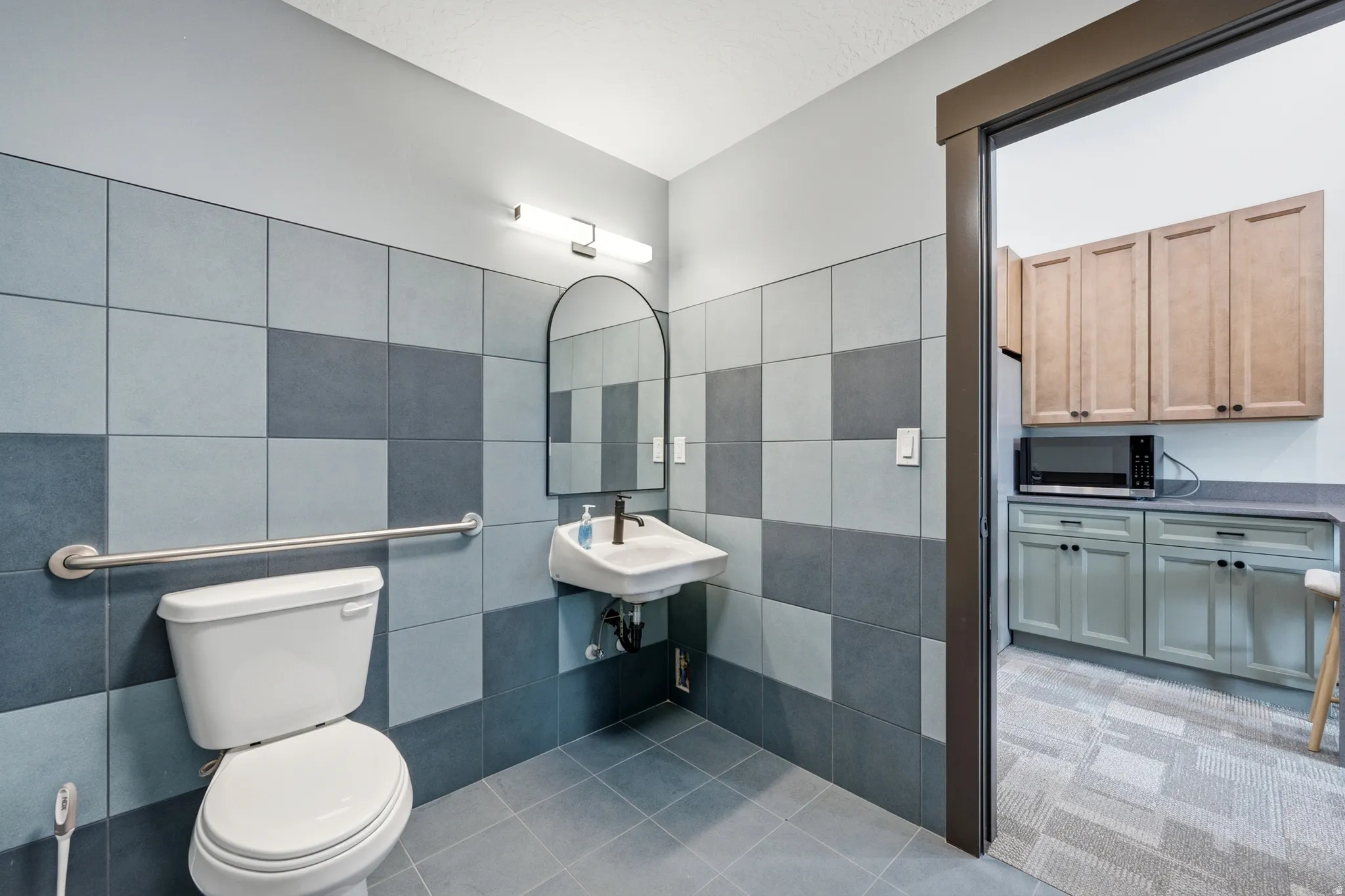 Patterned wall tiling with contrasting light and dark blue tones, complemented by a floor-mounted toilet, wall-mounted sink, and an arched mirror