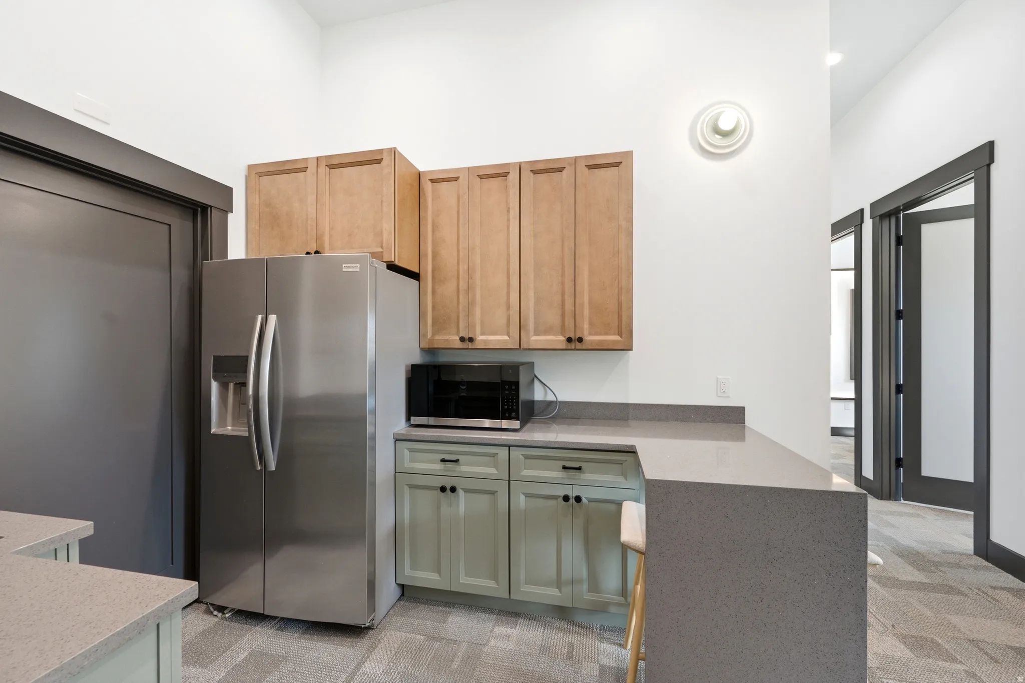 Stainless steel refrigerator, light wood-finish upper cabinetry, light green lower cabinetry, and expansive grey countertops