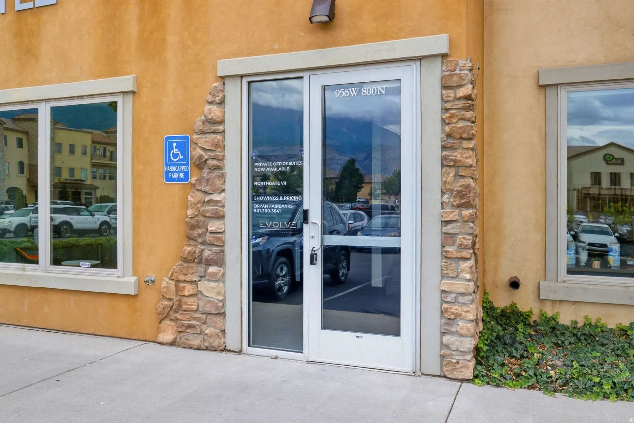 Glass entry door with side lite, stone veneer accents, and stucco exterior