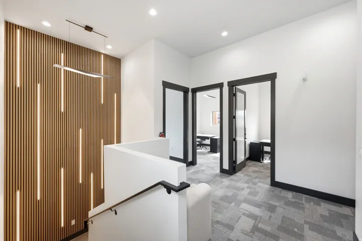 Wood-finish slat wall with integrated lighting, modern pendant light fixture, white walls, dark framed glass-panel doors, and patterned carpet flooring